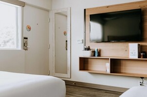 Ein Hotelzimmer mit einem großen Flachbildfernseher an einer Holzwand, einem Nachttisch mit einer Wasserflasche und einer Tür mit Griff.