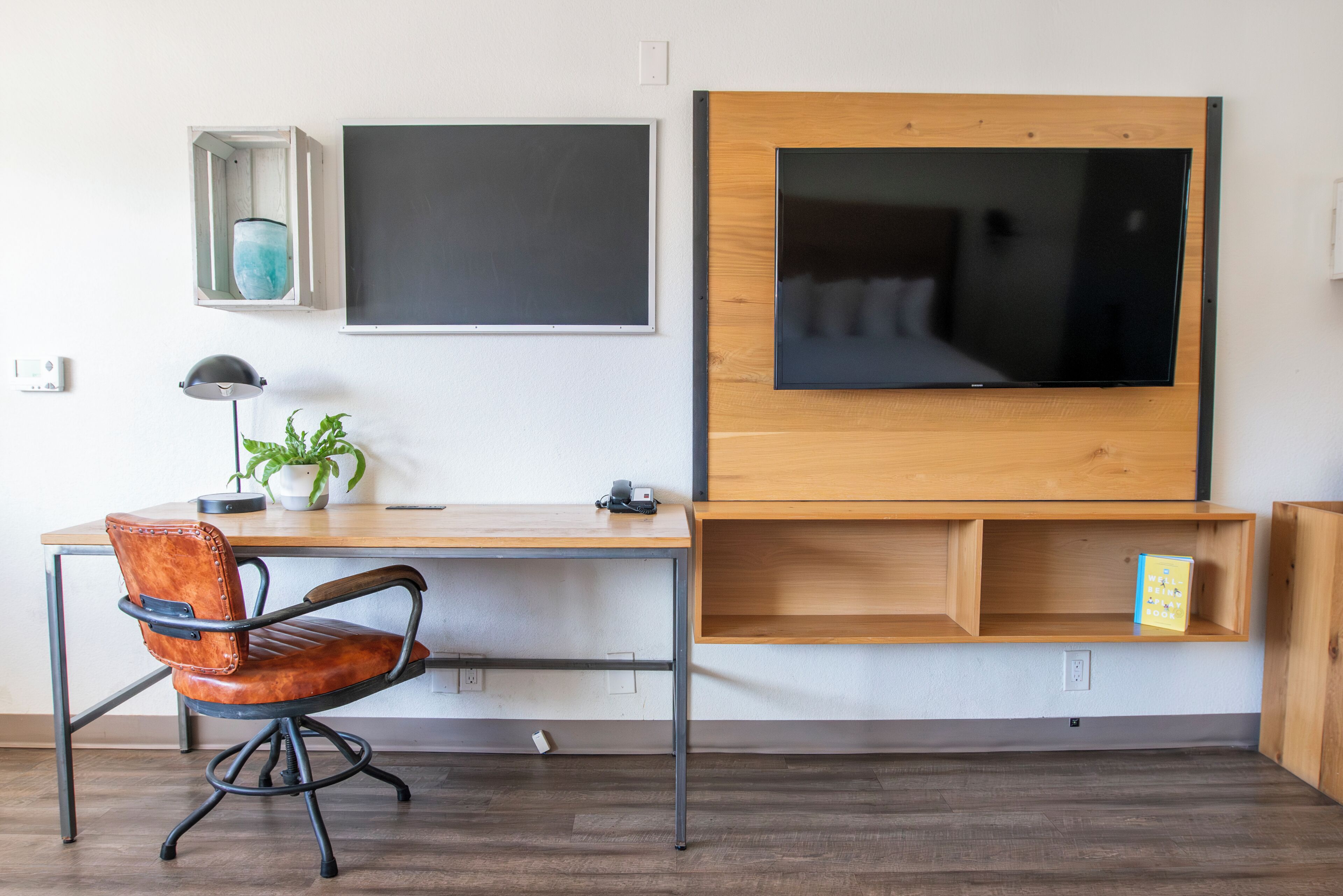 Een moderne kantoorruimte met een bureau, stoel, computermonitor en een groot flatscreen beeldscherm bevestigd aan een houten wand.