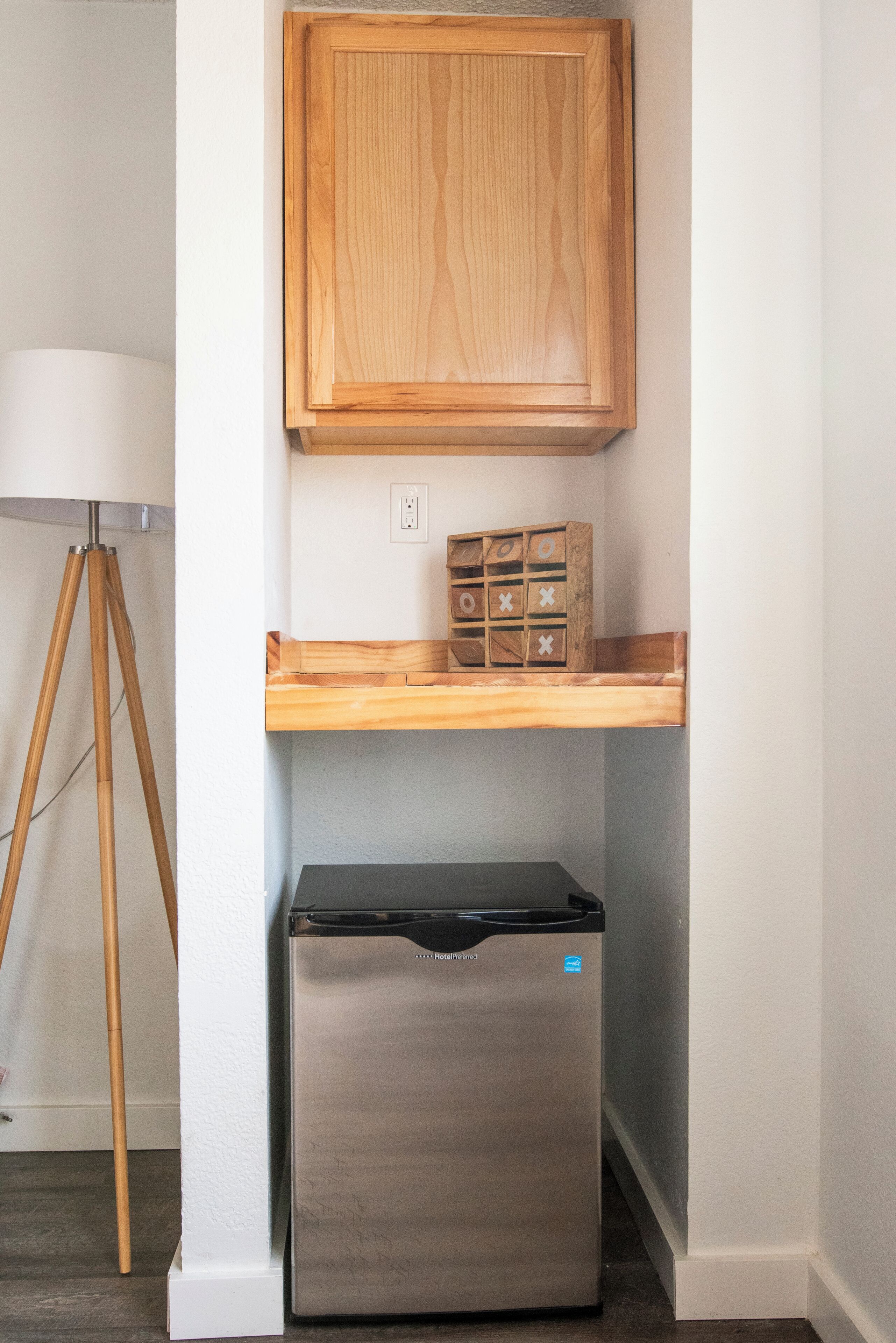 A compact kitchen with a wooden cabinet, a small wooden shelf, and a black refrigerator.