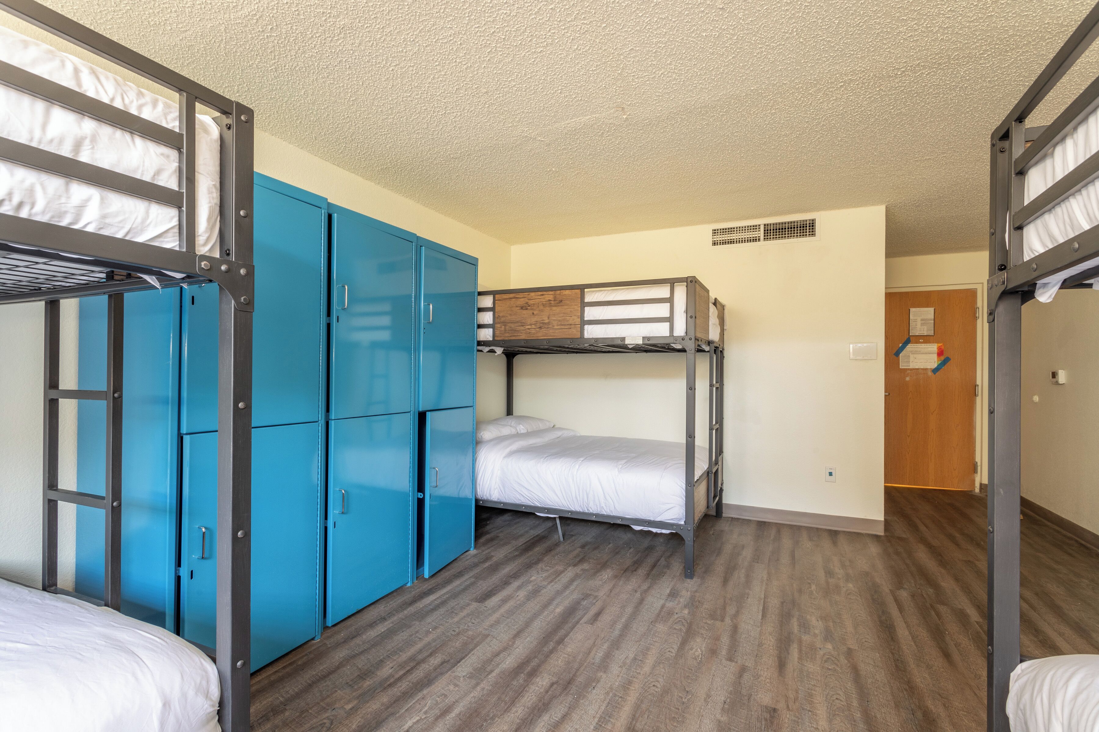 A dormitory room with bunk beds, a blue wardrobe, and a wooden floor.