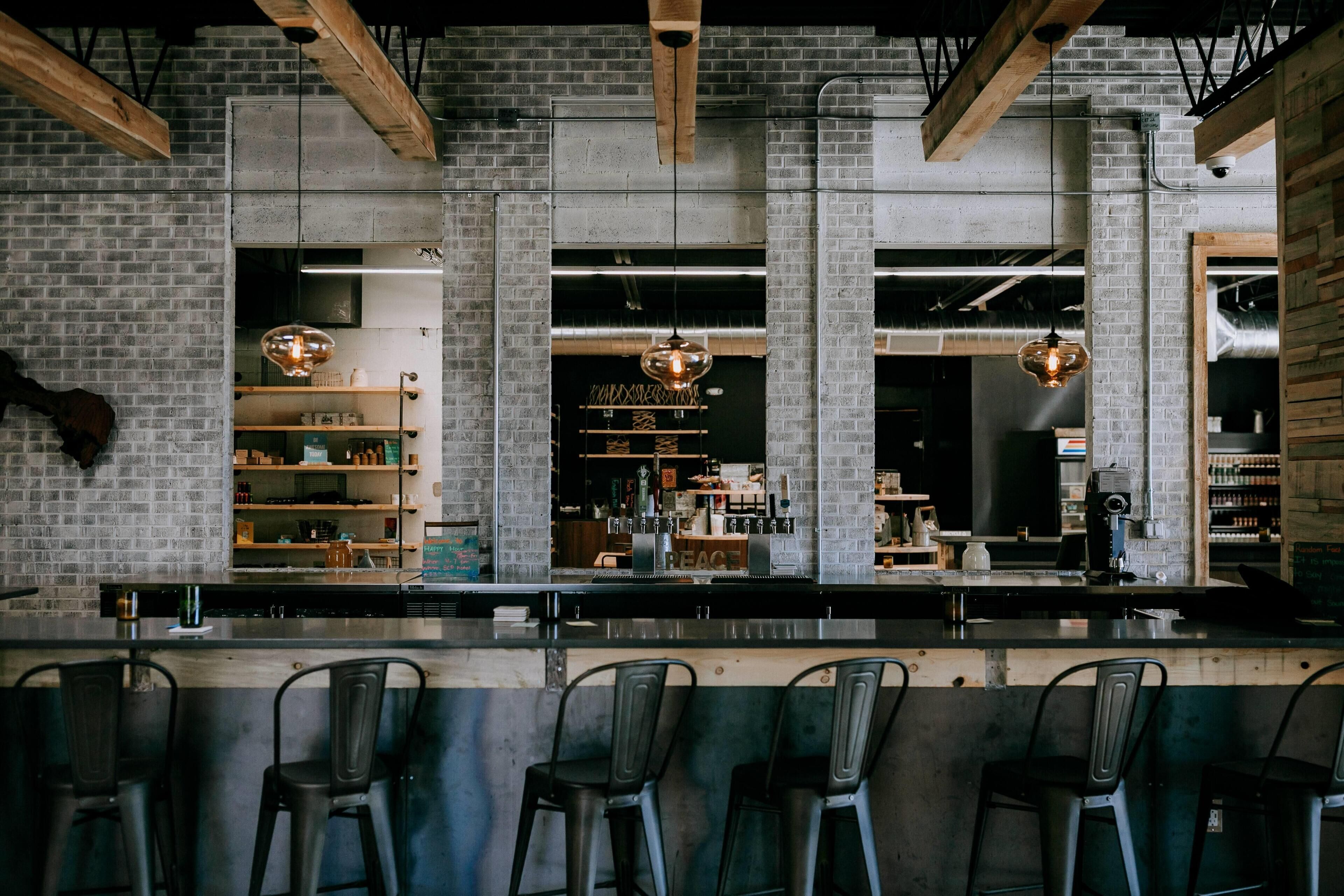 A bar area with a brick wall, wooden beams, and hanging pendant lights.