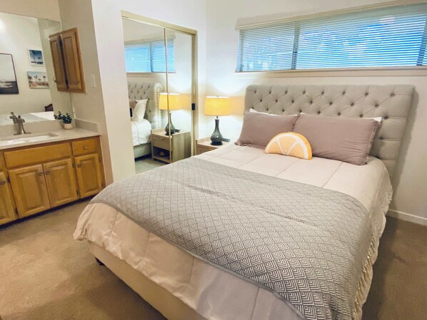 Un dormitorio con una cama grande, una mesita de noche con lámpara, un espejo, un armario y una ventana con persianas.