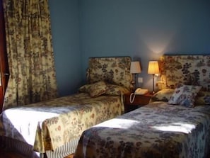 A room with two beds, floral bedspreads, a nightstand with a lamp, and a telephone. - Hotel Rural La Puerta de la Ribera (Sardon de Duero)