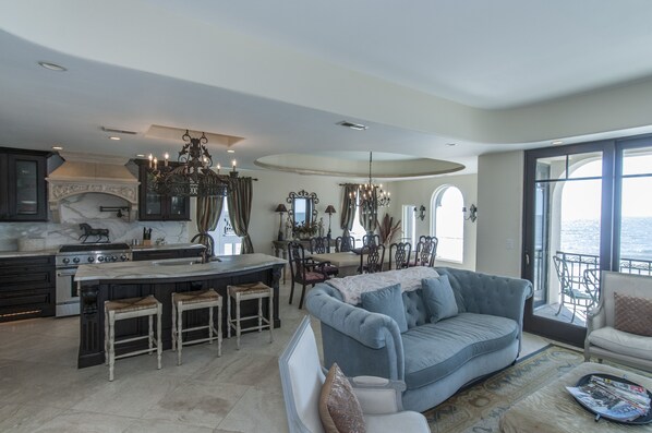 A spacious living area with a large sofa, a dining table, and a kitchen with a marble countertop.