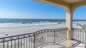 Vue sur la plage depuis un balcon couvert doté d’une balustrade, avec vue sur l’océan et la plage de sable.