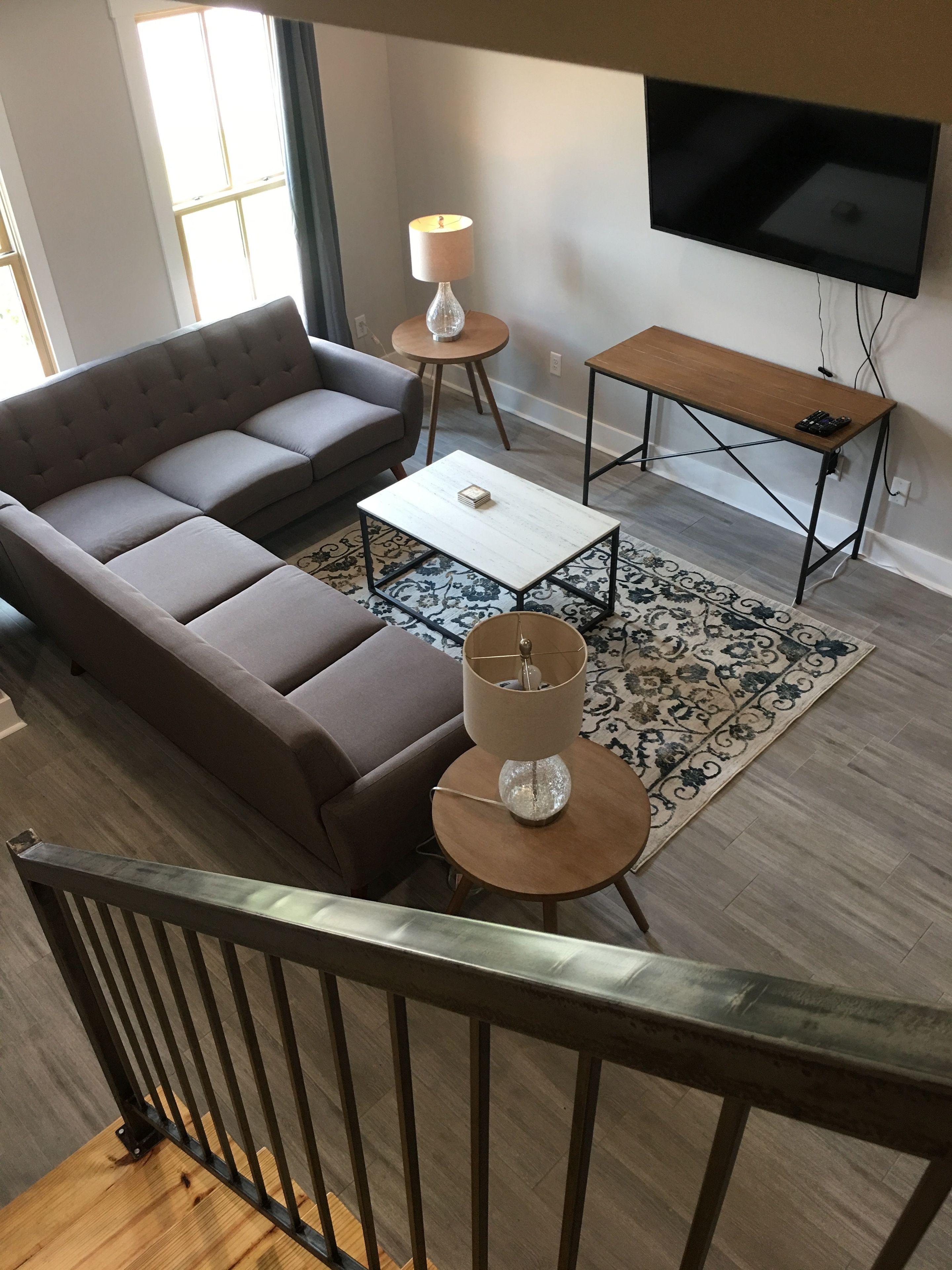 Una sala moderna con un sofá modular, una mesa de centro, una mesita auxiliar con una lámpara, un televisor montado en la pared y piso de madera.