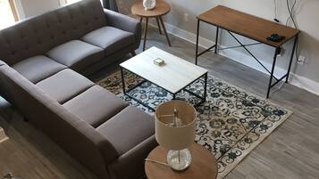 Una sala moderna con un sofá modular, una mesa de centro, una mesita auxiliar con una lámpara, un televisor montado en la pared y piso de madera.