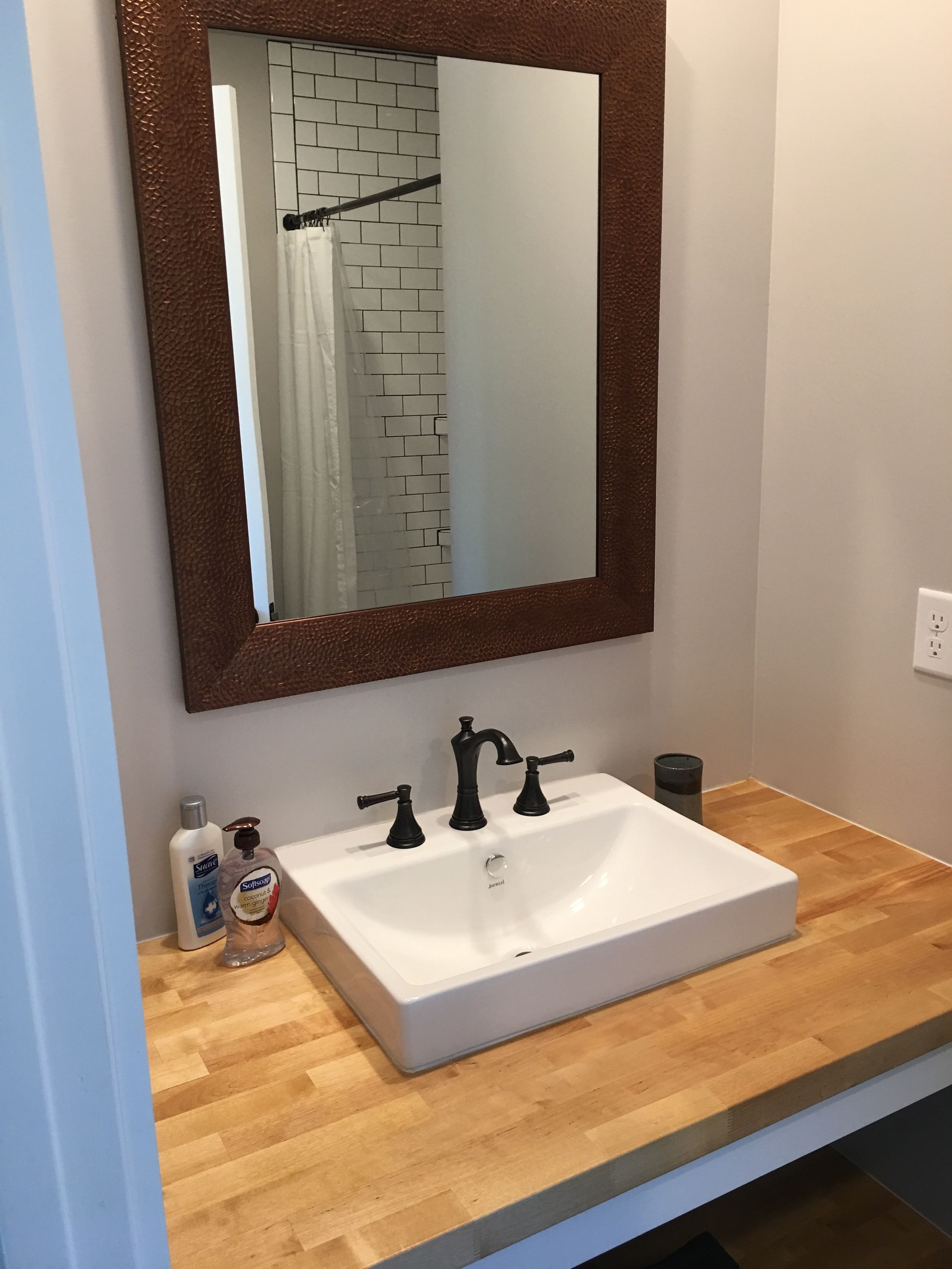 A bathroom with a white sink, black faucets, and a brown-framed mirror.