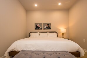 A bedroom with a large bed, a bedside table with a lamp, and two wall-mounted artworks.