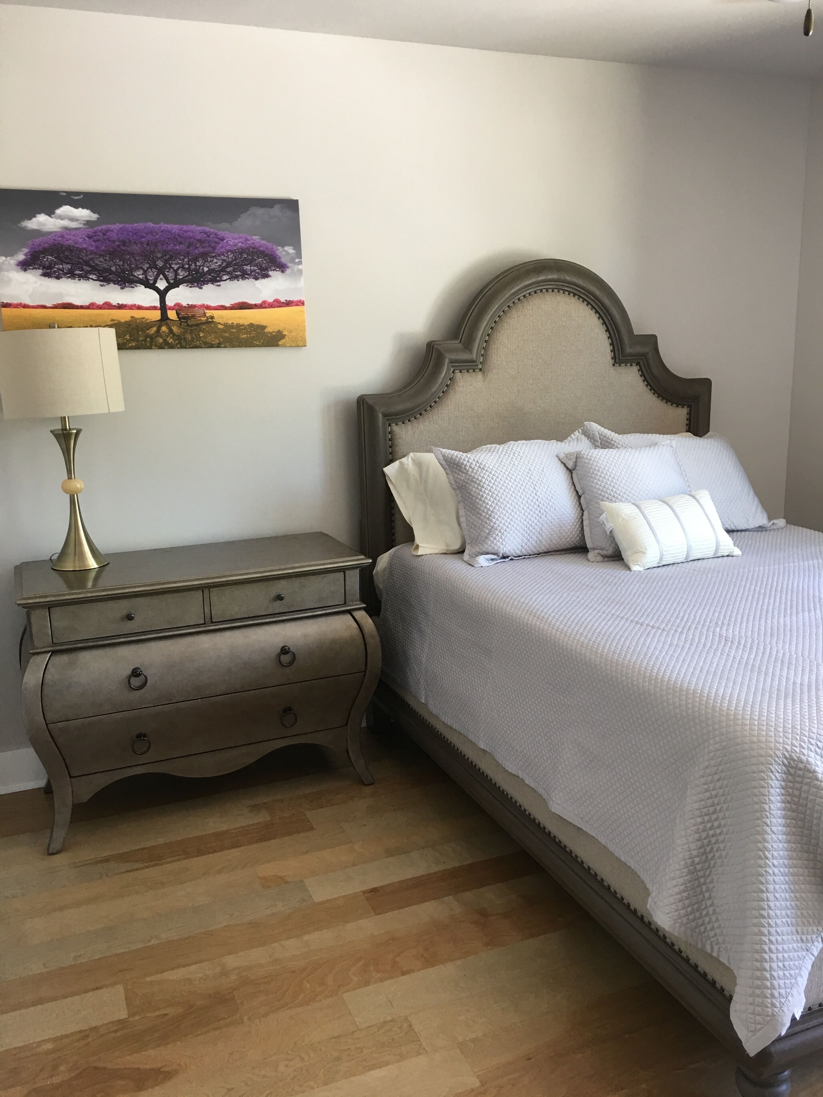 A bedroom with a bed, a nightstand, a lamp, and a painting on the wall.