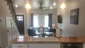 A modern kitchen with a wooden countertop, white cabinets, a stainless steel dishwasher, and a ceiling fan. - The Hotel at Huntington Square (Jonesboro)