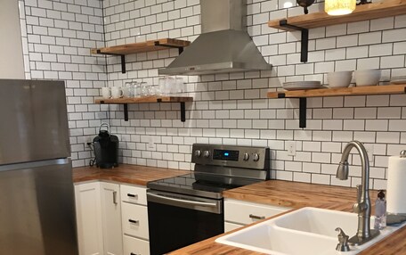 A modern kitchen with white subway tiles, a stainless steel refrigerator, a wooden countertop, and a built-in oven.