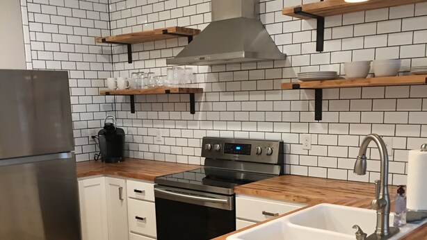 A modern kitchen with white subway tiles, a stainless steel refrigerator, a wooden countertop, and a built-in oven. - The Hotel at Huntington Square (Jonesboro)