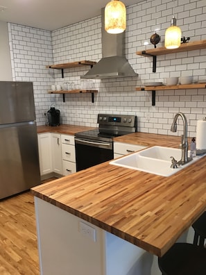 A modern kitchen with white subway tiles, a stainless steel refrigerator, a wooden countertop, and a built-in oven.