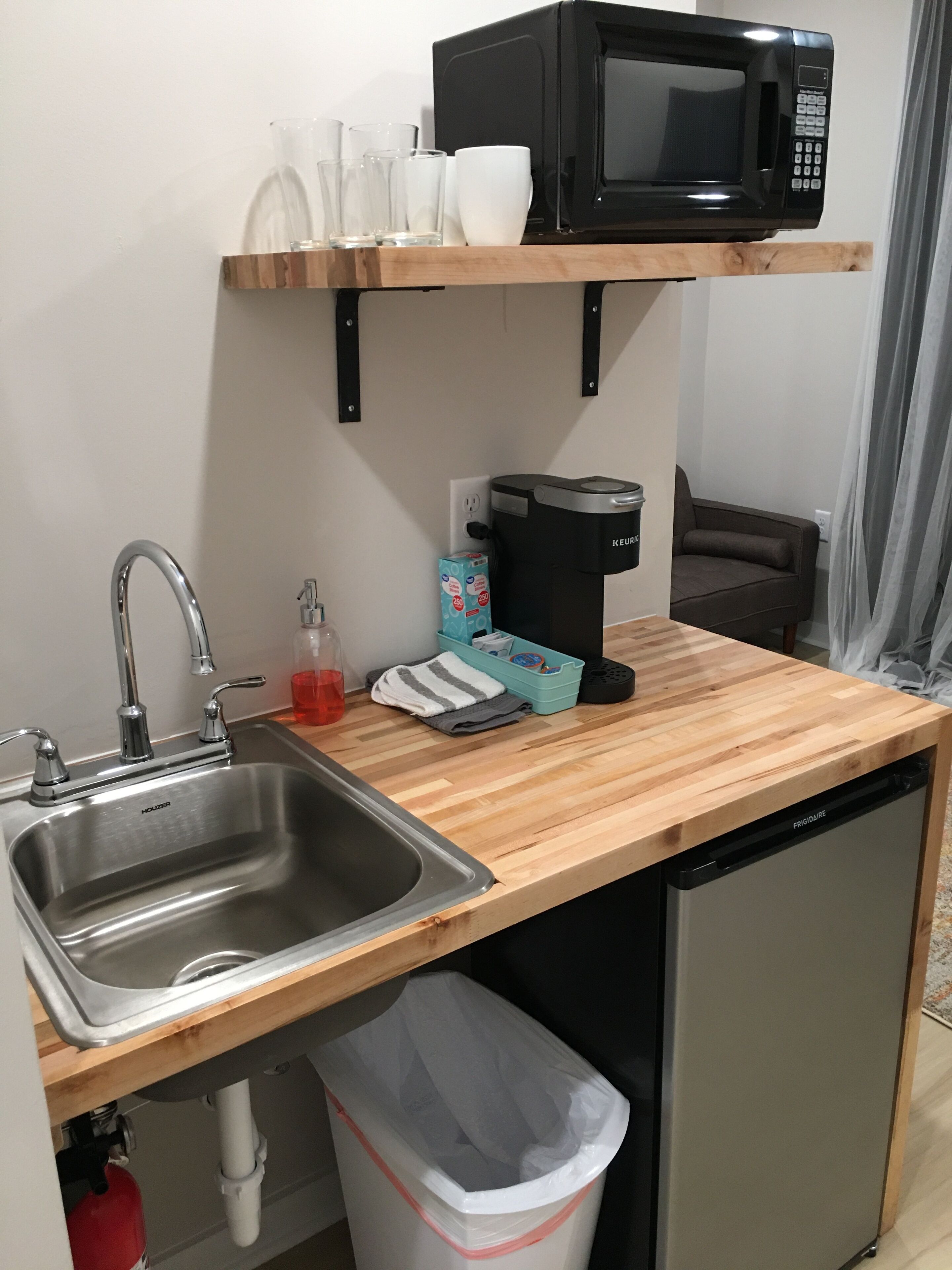 A compact kitchen with a stainless steel sink, a black coffee maker, a microwave, and a dishwasher.