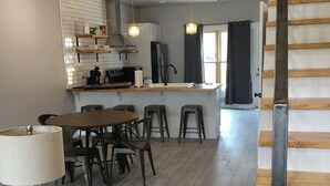 A modern kitchen with a dining area, wooden flooring, and pendant lighting. - The Hotel at Huntington Square (Jonesboro)