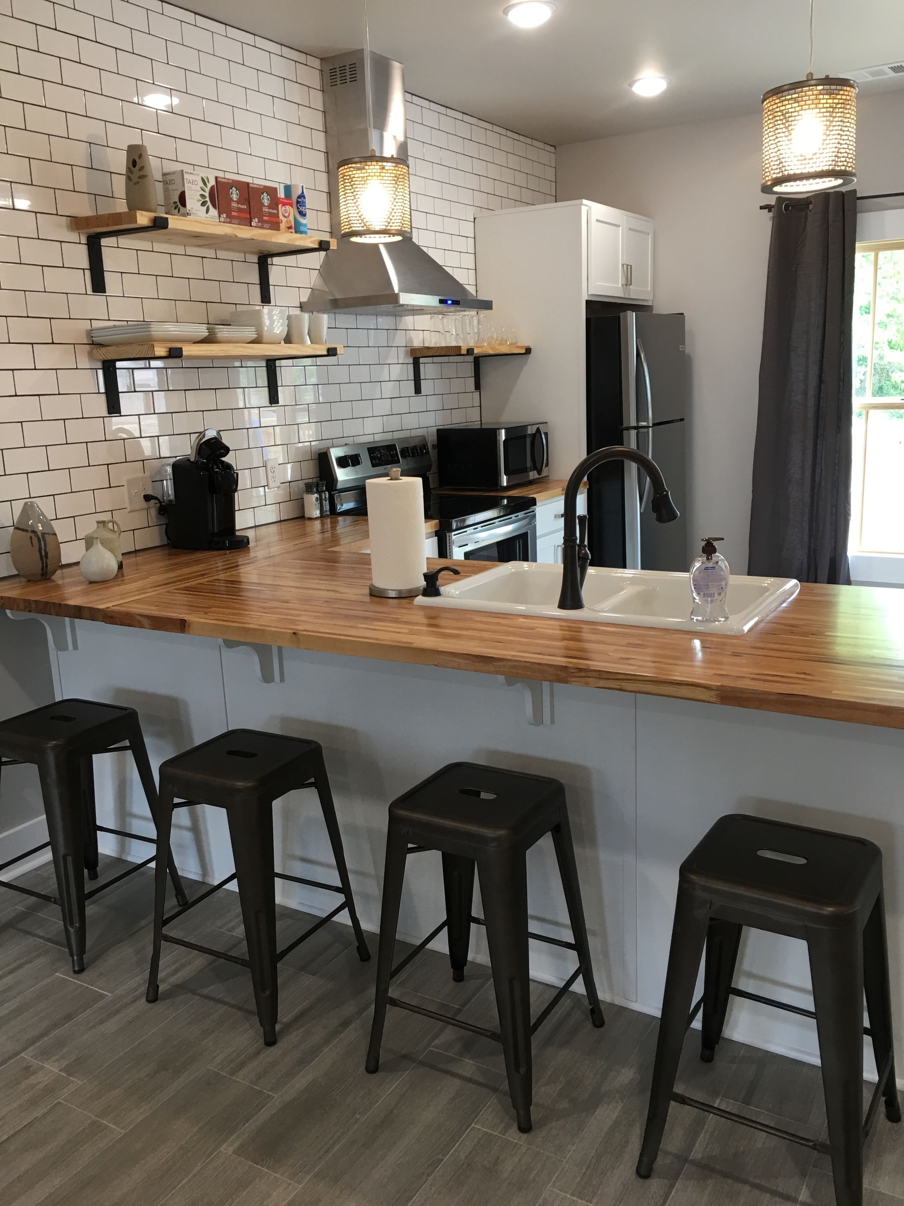A modern kitchen with a wooden countertop, stainless steel appliances, a built-in sink, and bar stools.