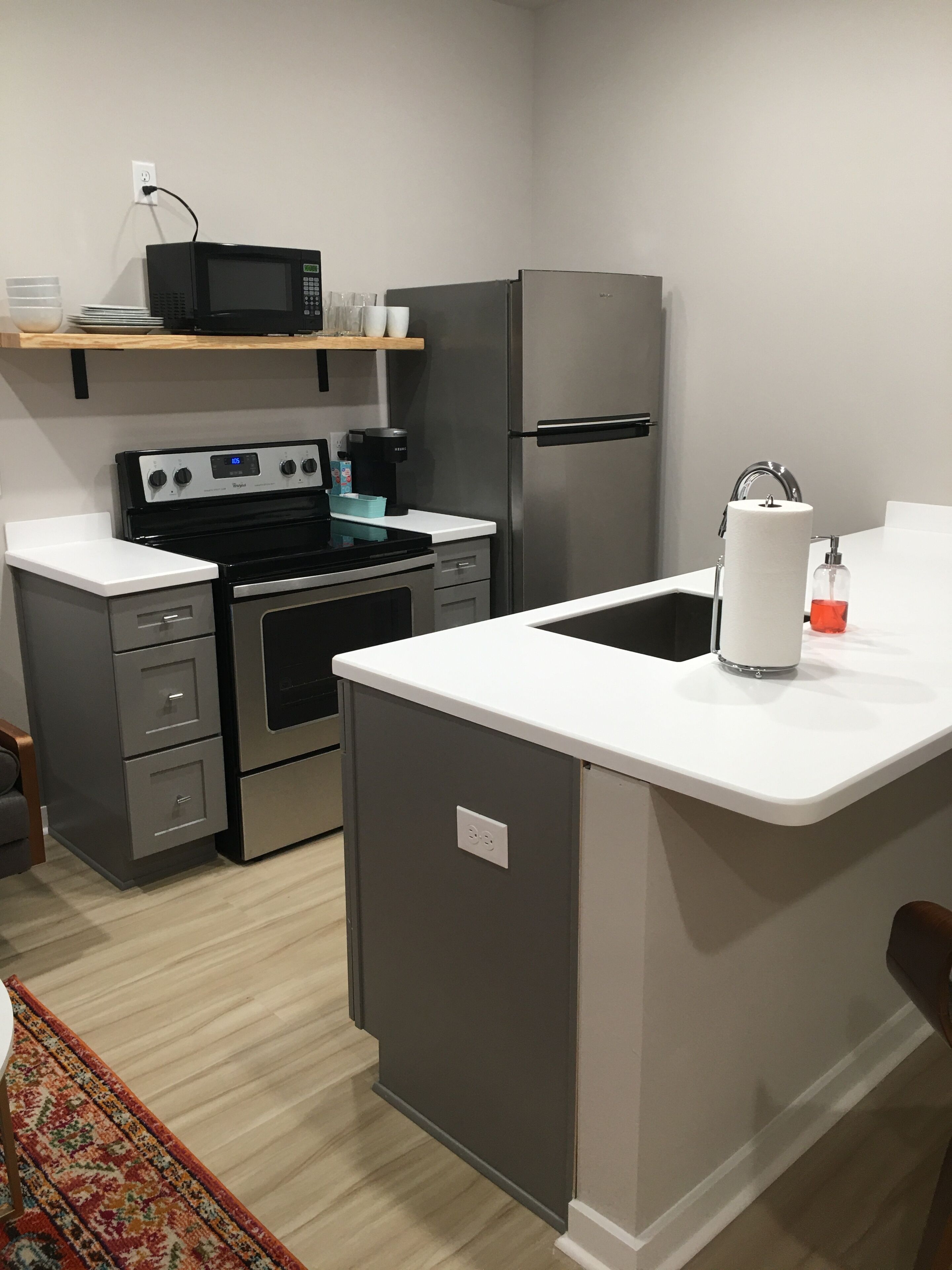Una cocina compacta equipada con estufa, microondas, refrigerador y un lavamanos pequeño.