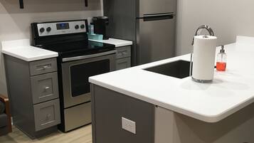 Una cocina compacta equipada con estufa, microondas, refrigerador y un lavamanos pequeño.