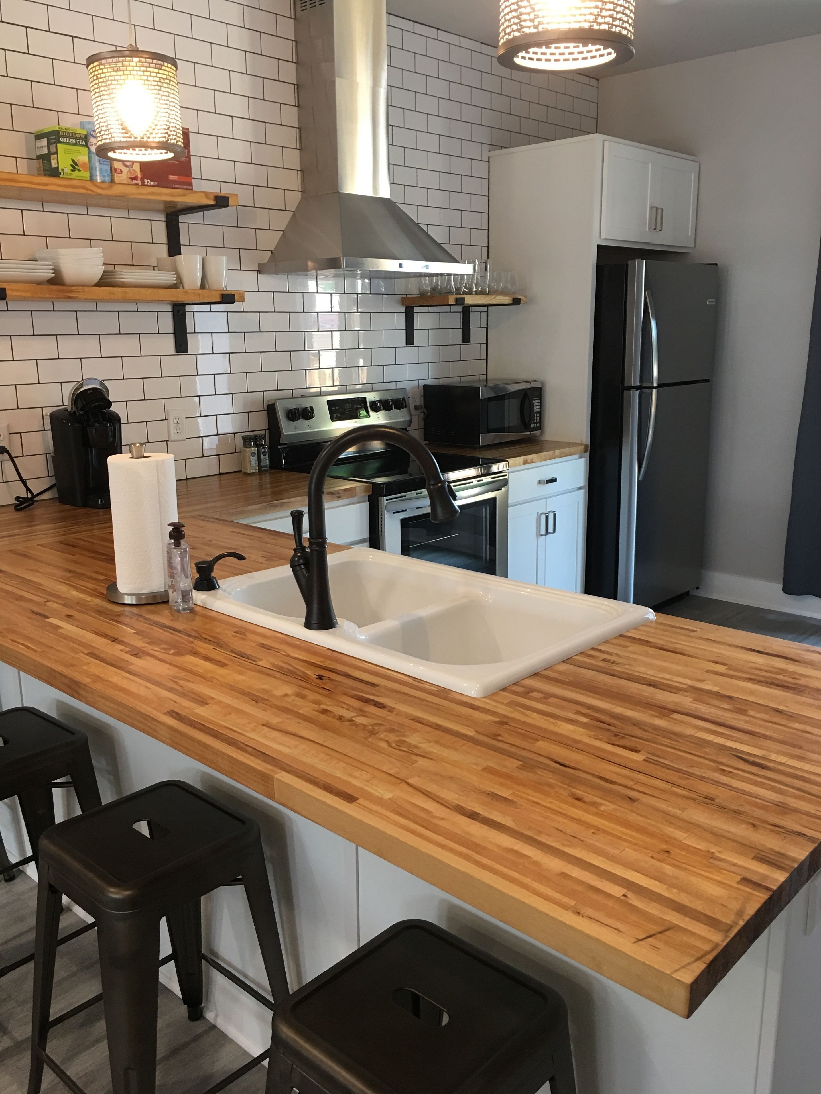 A modern kitchen with a wooden countertop, stainless steel appliances, a double sink, and bar stools.