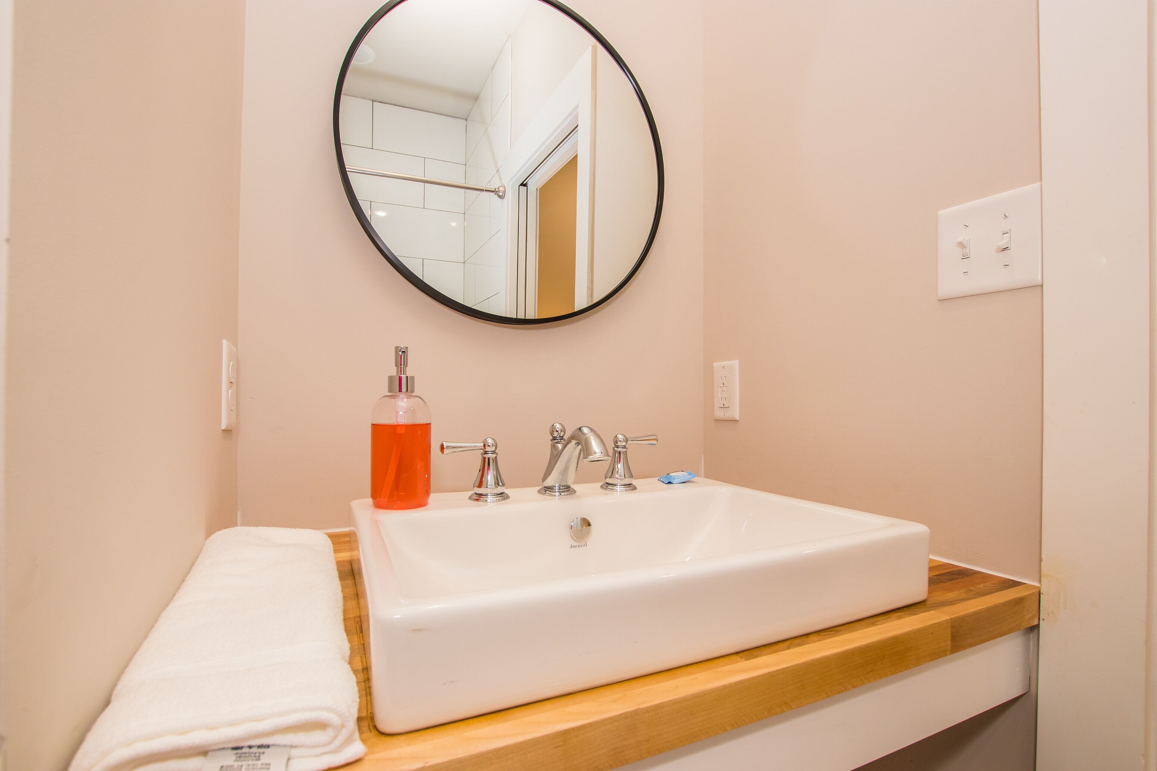 Un baño con un lavamanos blanco, un espejo redondo y una encimera de madera.