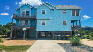 A two-story building with a blue exterior, a balcony on the first floor, and a covered entrance area. - 3rd row Whalehead house w/ private pool, hot tub, elevator, pool table, pet friendly (Corolla)