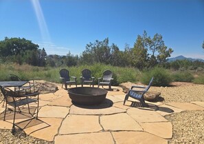 Relax in the serene outdoor patio, surrounded by trees and featuring a fire pit and Adirondack chairs.