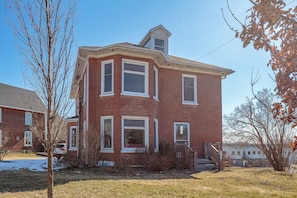 A two-story brick house with a gabled roof, a front porch, and a visible chimney.