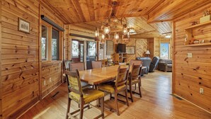 Interior de una cabaña de madera con una mesa de comedor, sillas, un sofá y un televisor.