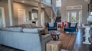 A spacious living area with a grey sofa, two armchairs, a coffee table, and a staircase leading to an upper level. - Spacious, budget friendly 3 BR House! (Gulf Shores)
