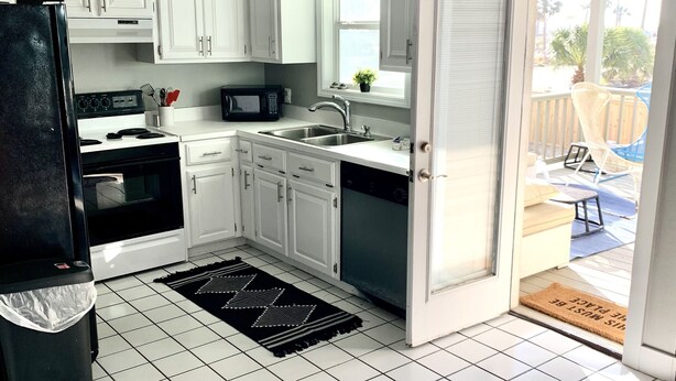 A kitchen with white cabinets, a black refrigerator, a microwave, and a sink. - Spacious, budget friendly 3 BR House! (Gulf Shores)