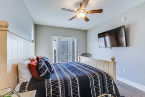A bedroom with a bed, a ceiling fan, a TV mounted on the wall, and a door leading to an outdoor area.