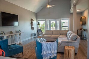 A spacious living room with a large sectional sofa, a flat-screen TV mounted on the wall, and a ceiling fan.