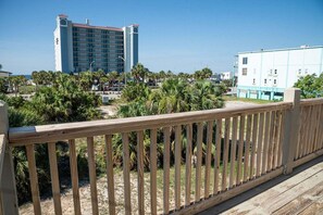 A beachfront hotel with a wooden deck, palm trees, and a clear view of the ocean.