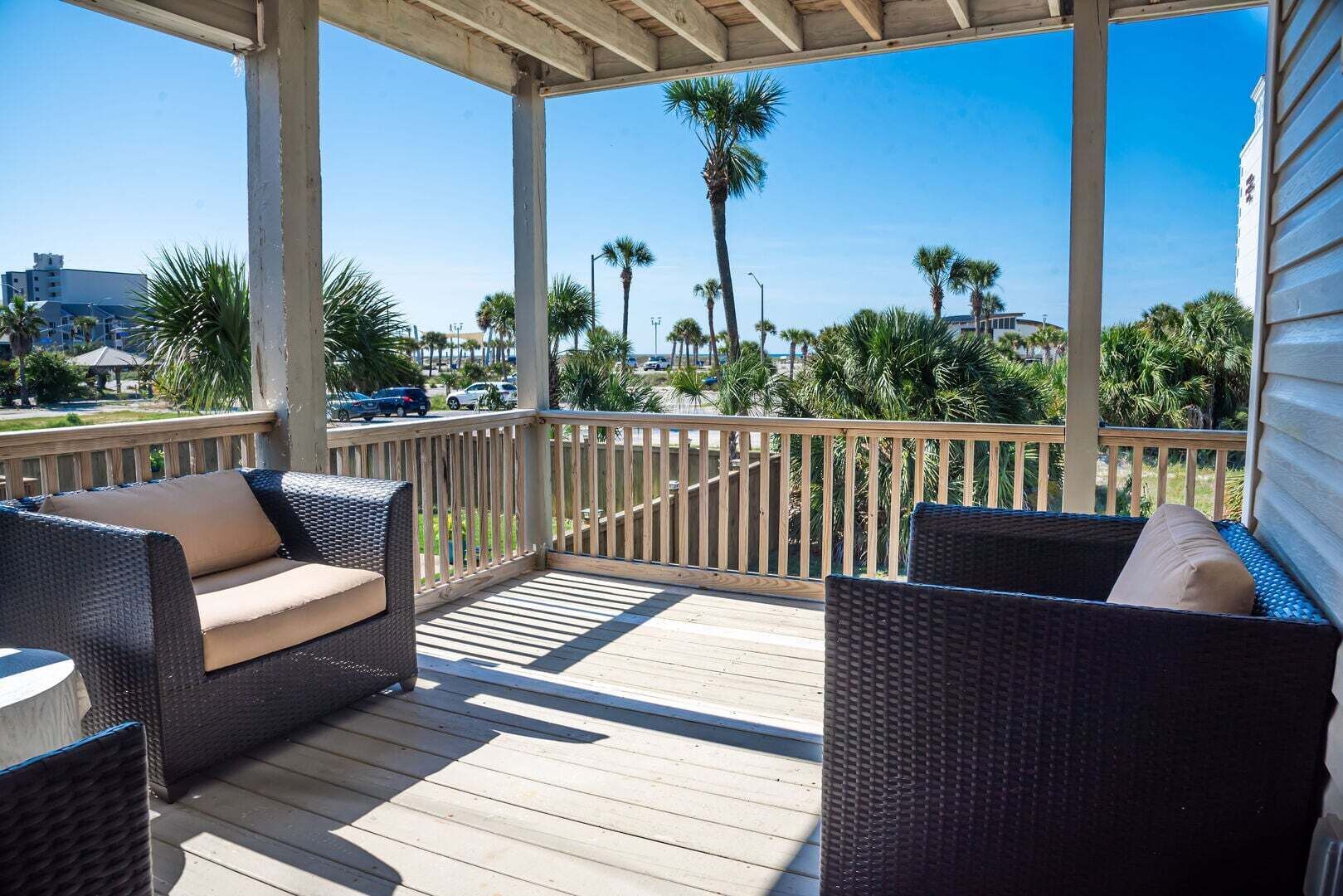 Un espace extérieur abrité, aménagé avec des meubles en osier et offrant une vue sur les palmiers et les bâtiments.