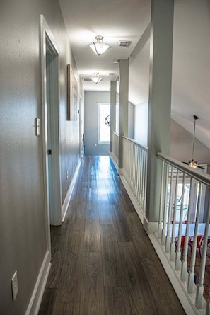 A hallway with wooden flooring, white railings, and ceiling lights.