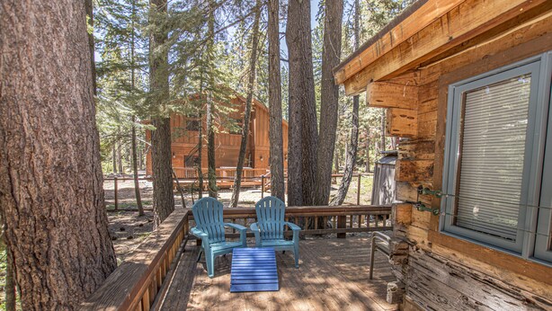 Una cabaña de madera con un porche, dos sillas Adirondack y un banco.