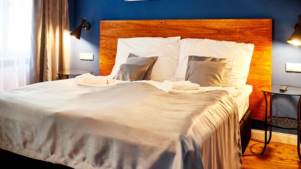 Un lit bien fait, avec du linge de lit blanc et des oreillers, une tête de lit en bois et une table de chevet avec une lampe.