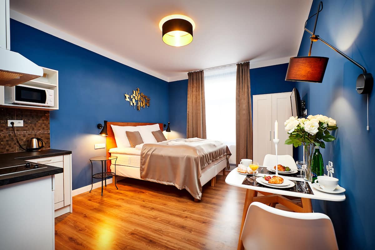 A modern hotel room with a bed, a dining table with breakfast, a microwave, and a small kitchen area.
