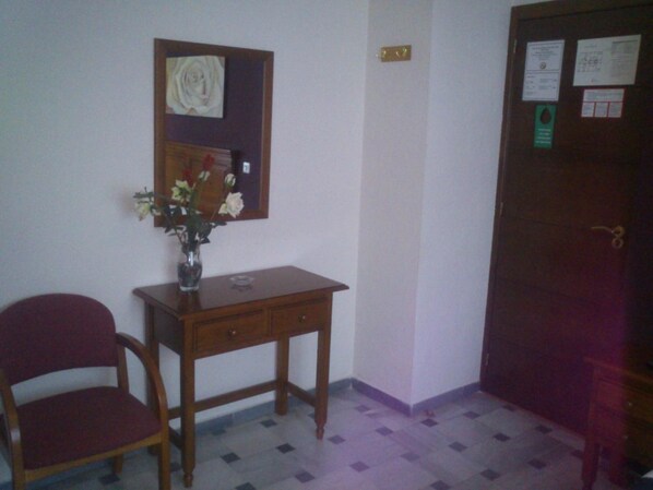 A room with a wooden desk, a chair, a vase with flowers, a framed picture on the wall, and a door with notices. - Hostal Cabrera (Motril)
