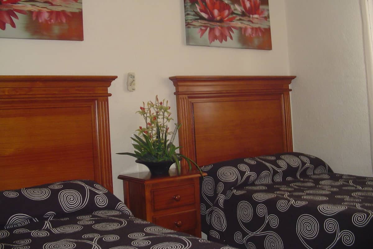 A bedroom with two beds, a nightstand, and a potted plant.