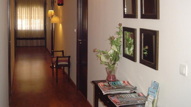 A hallway with a wooden floor, a chair, a table with magazines, a vase with flowers, and framed pictures on the wall. - Hostal Cabrera (Motril)