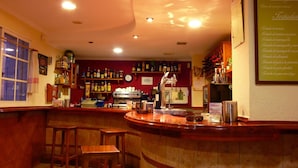 A bar area with wooden stools, a counter, and shelves stocked with bottles. - Hostal Cabrera (Motril)