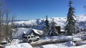 Un paysage montagneux enneigé avec une cabane et un VUS blanc garé devant.