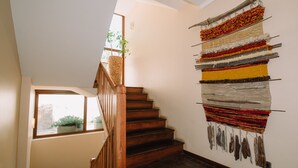 Un escalier avec des marches en bois menant à un palier, une œuvre d’art textile accrochée au mur et une fenêtre donnant sur un paysage verdoyant.