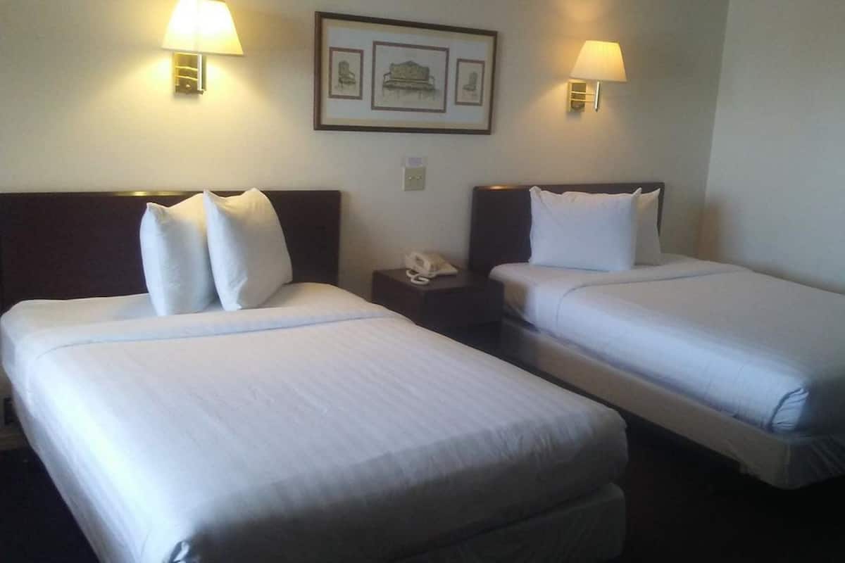 A hotel room with two single beds, each with white linens, a nightstand with a phone, and wall-mounted lamps.