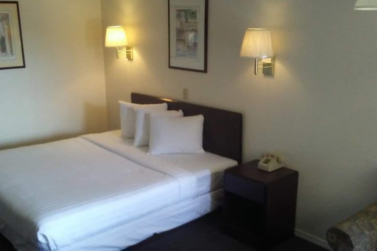A hotel room with a large bed, two bedside lamps, a nightstand with a phone, and a framed picture on the wall.