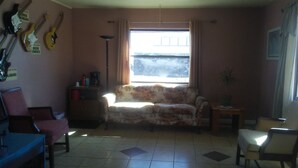 Ein Wohnzimmer mit einer Couch, einem Couchtisch, einer Lampe und einer Topfpflanze. Gitarren hängen an der Wand.