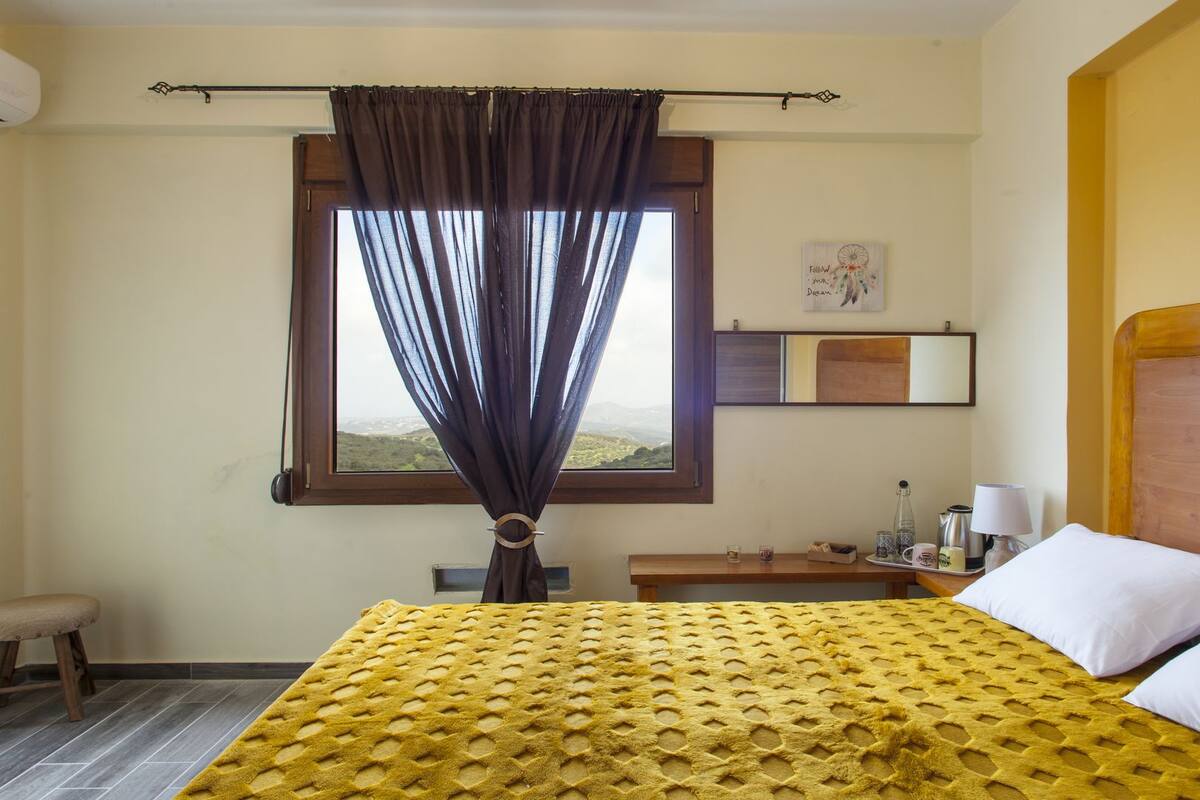 A hotel room with a bed, a nightstand, a lamp, and a window with curtains.