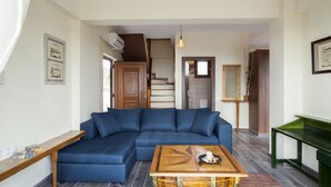 A modern living room with a blue sectional sofa, a wooden coffee table, and a staircase leading to an upper floor. - Foivos and Athina Villas (Archanes-Asterousia)